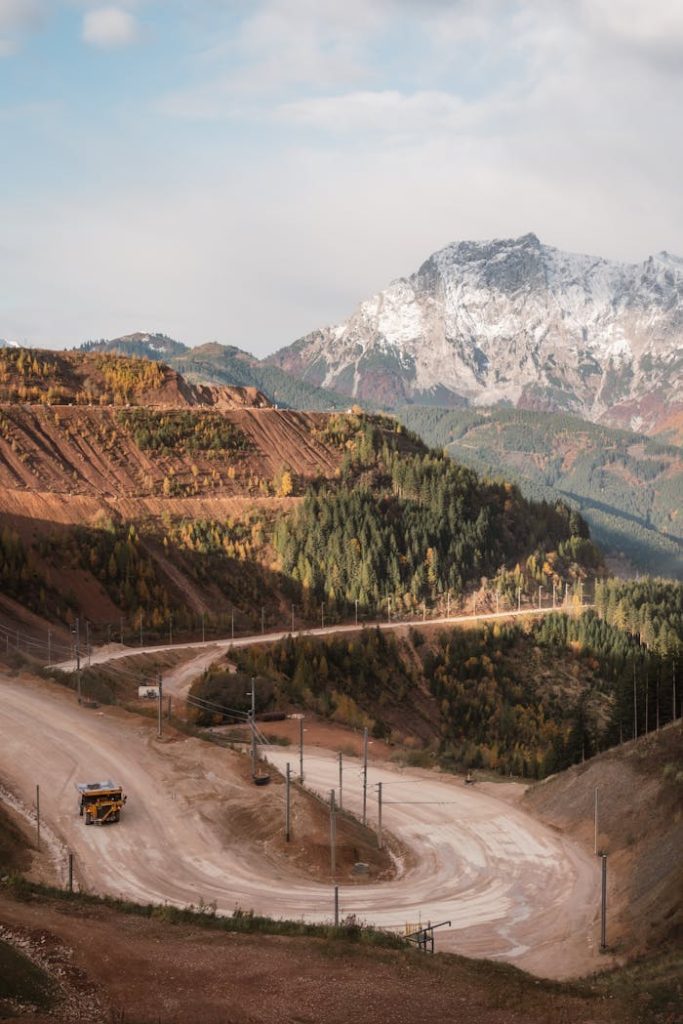 A large quarry with heavy machinery set against a scenic mountain landscape during autumn.